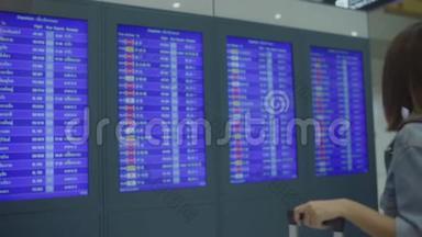 慢动作-快乐的亚洲女人看着信息板，用行李在候机大厅检查她的航班。
